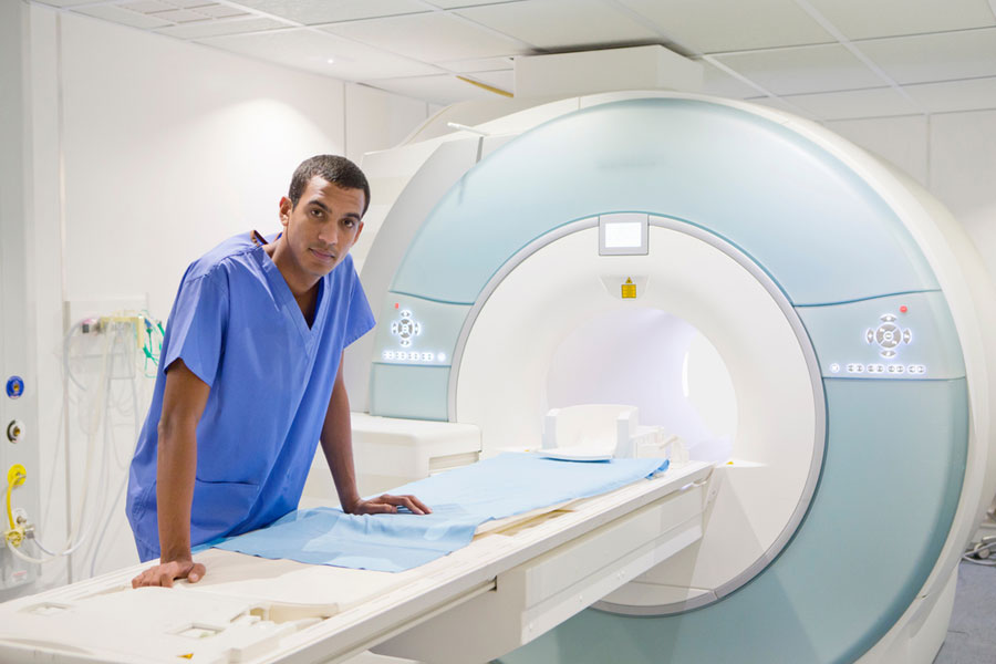 confident male MRI tech leans on an MRI machine in a hospital