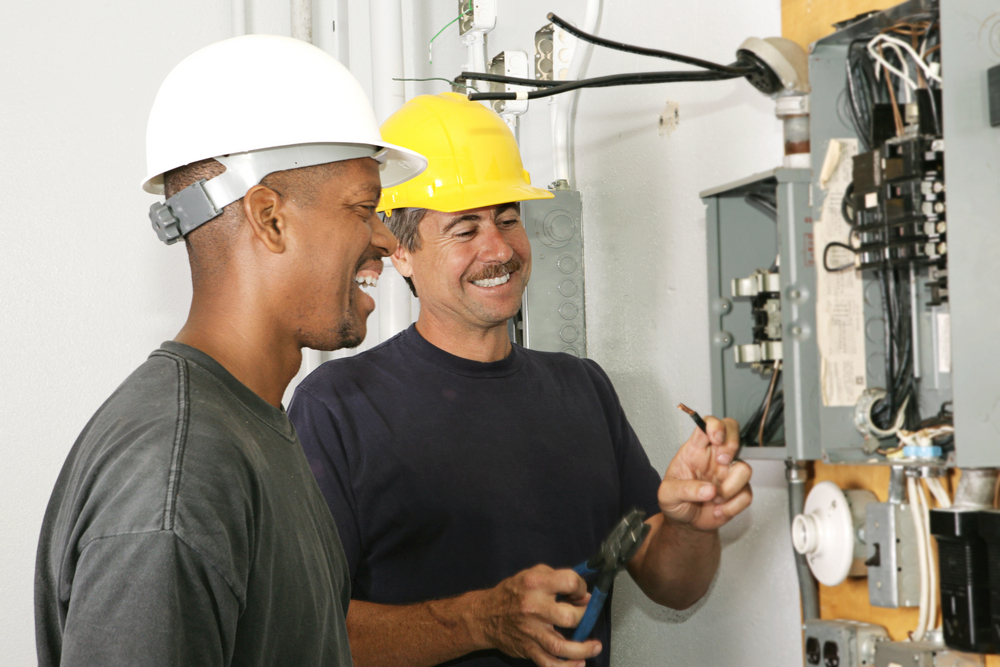 Two electricians work on an electrical panel. Electricians are among the highest paid trade jobs