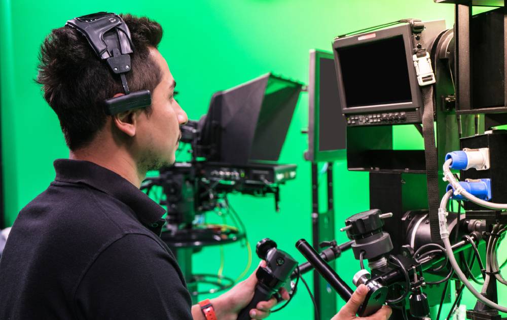 A communication professional works with broadcast equipment and cameras in front of a green screen.