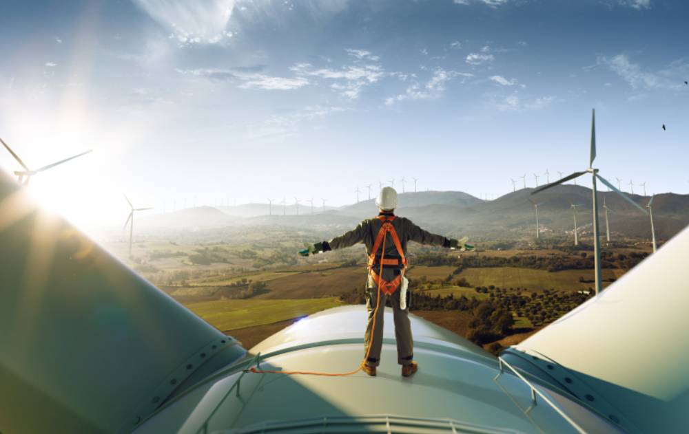 An energy professional stands on top of a wind turbine.