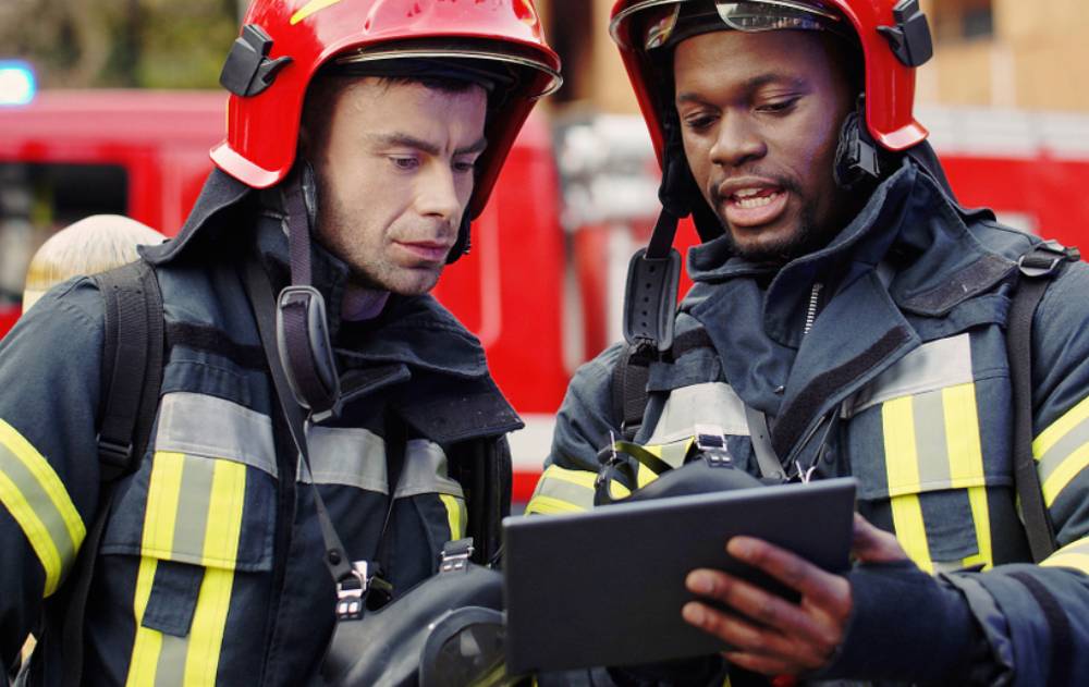 Two firefighters stand together, looking at a tablet device.
