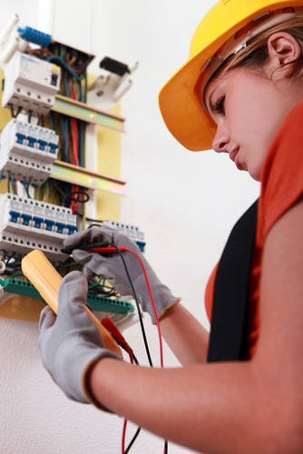 Young woman in a hardhat tests an electrical panel