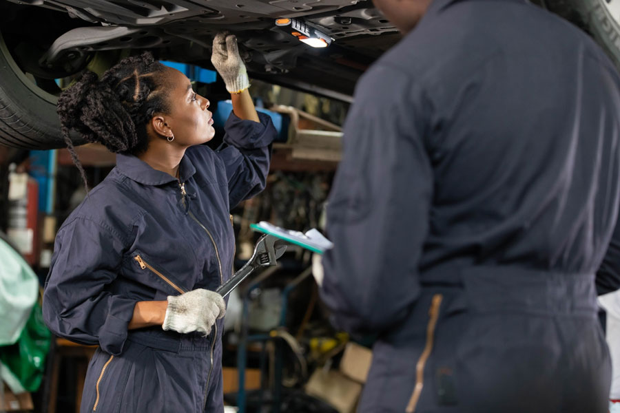 African female mechanic looks under a car in an auto repair shop