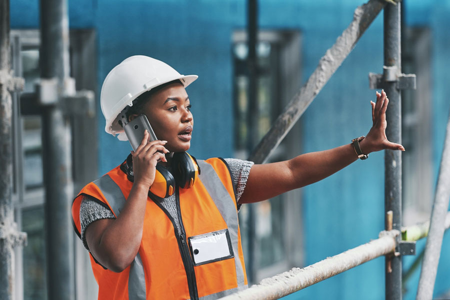 A Black female construction worker makes a call on a cellphone at a construction site. 