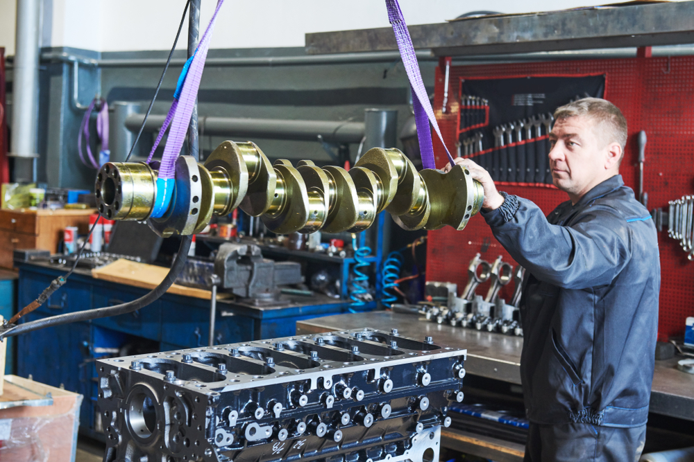 A diesel mechanic guides a crankshaft over to a diesel truck engine, example of diesel mechanic training
