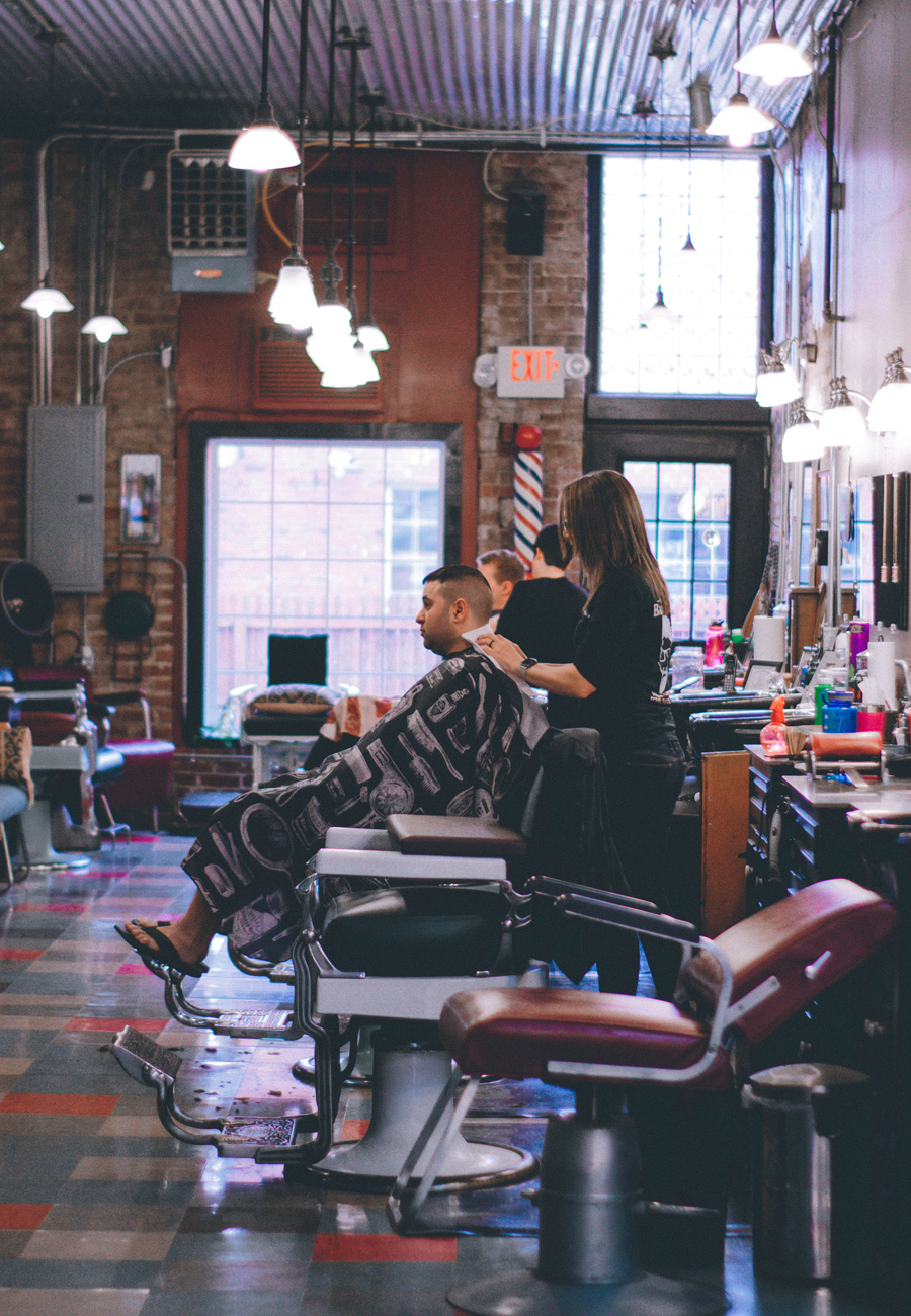 A female entrepreneur in a hair salon checks her notes before she cuts a client's hair. 
