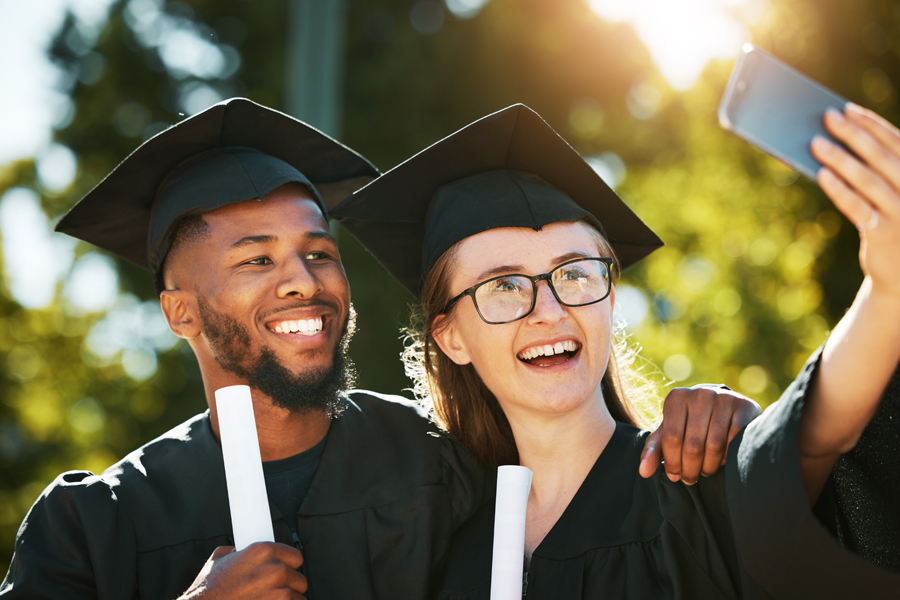 A white female student and a Black male student pose for a graduation selfie.