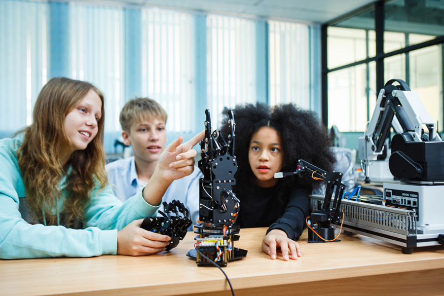 Three students tinker with a robotic arm to see how it works