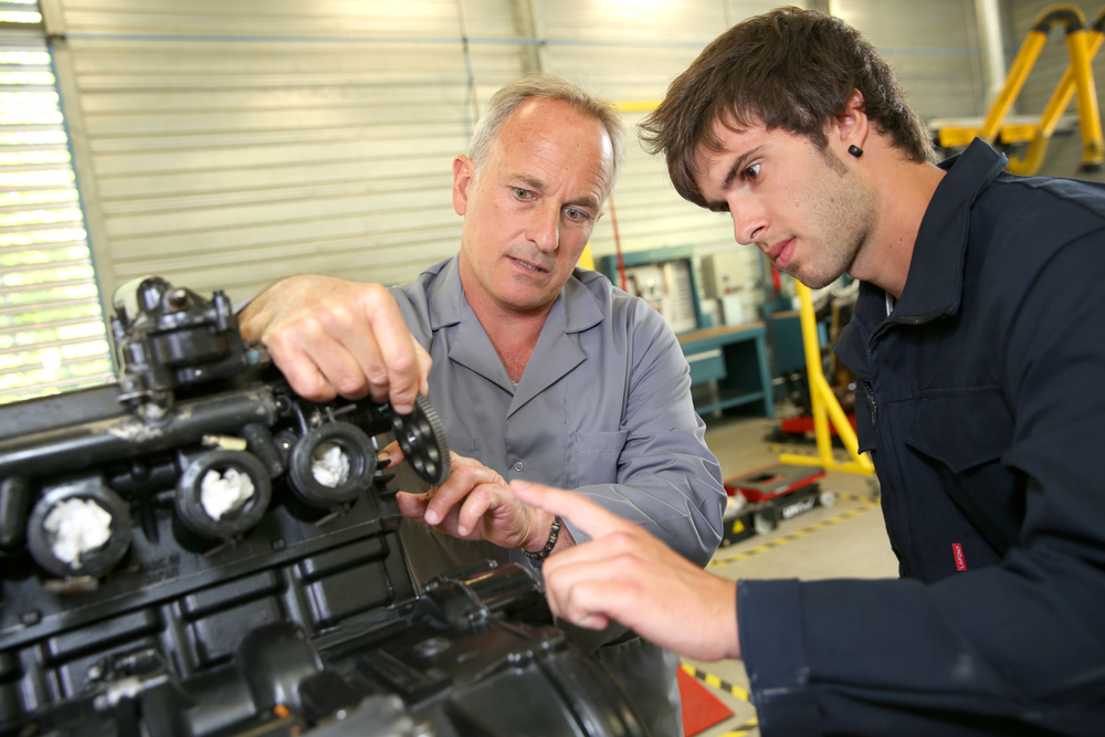 Older man teaches younger man in manufacturing setting, example of on the job training or apprenticeship