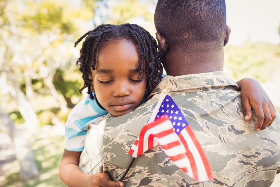 A young Black girl hugs her father, who's wearing a military uniform