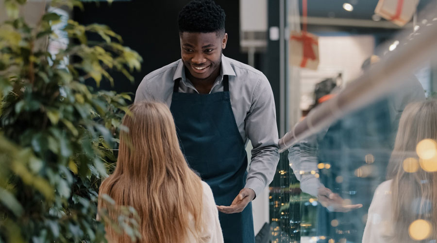 Young black man working at a cafe chats with a customer, a young White woman