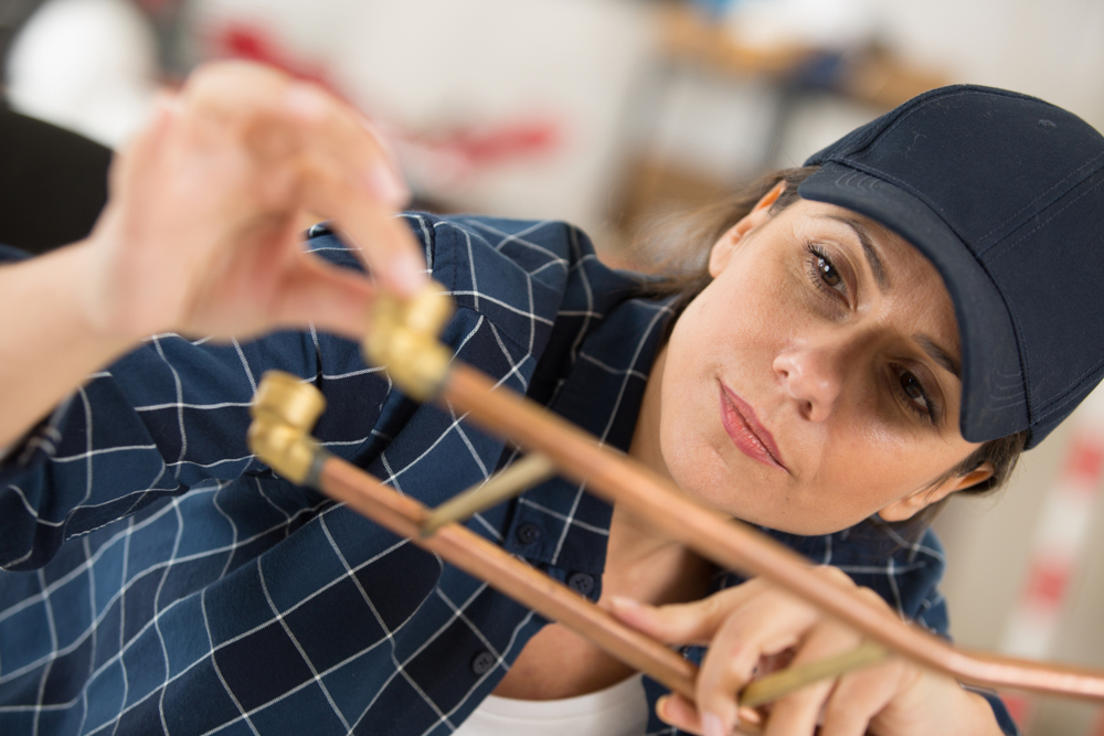 Female plumber working with copper pipe fittings. Plumbers are among the good-paying jobs that don't require a degree