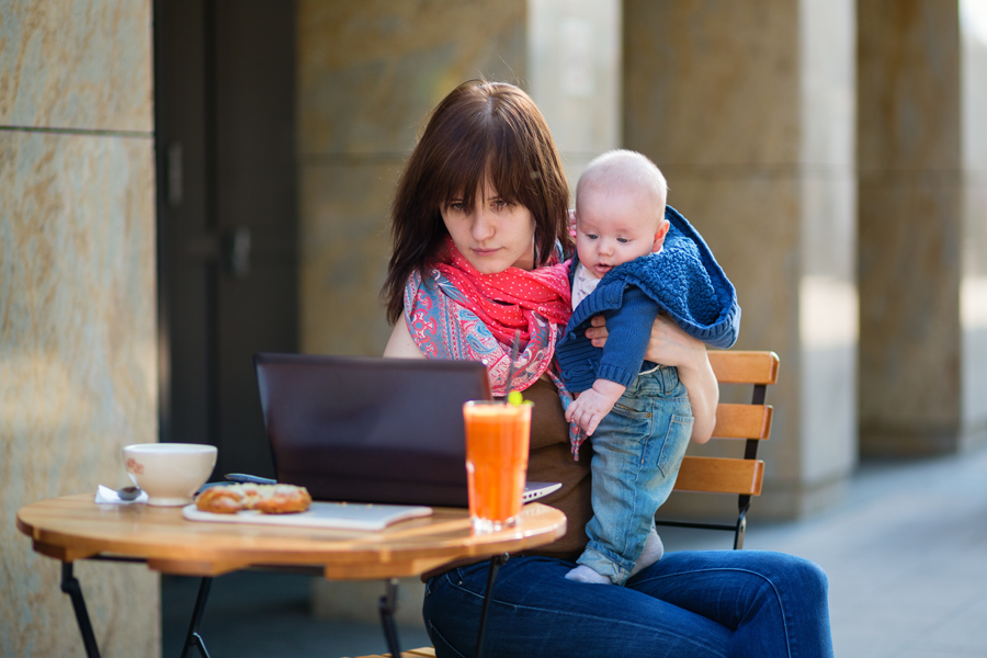 Young mom with a baby looks at her laptop at a cafe