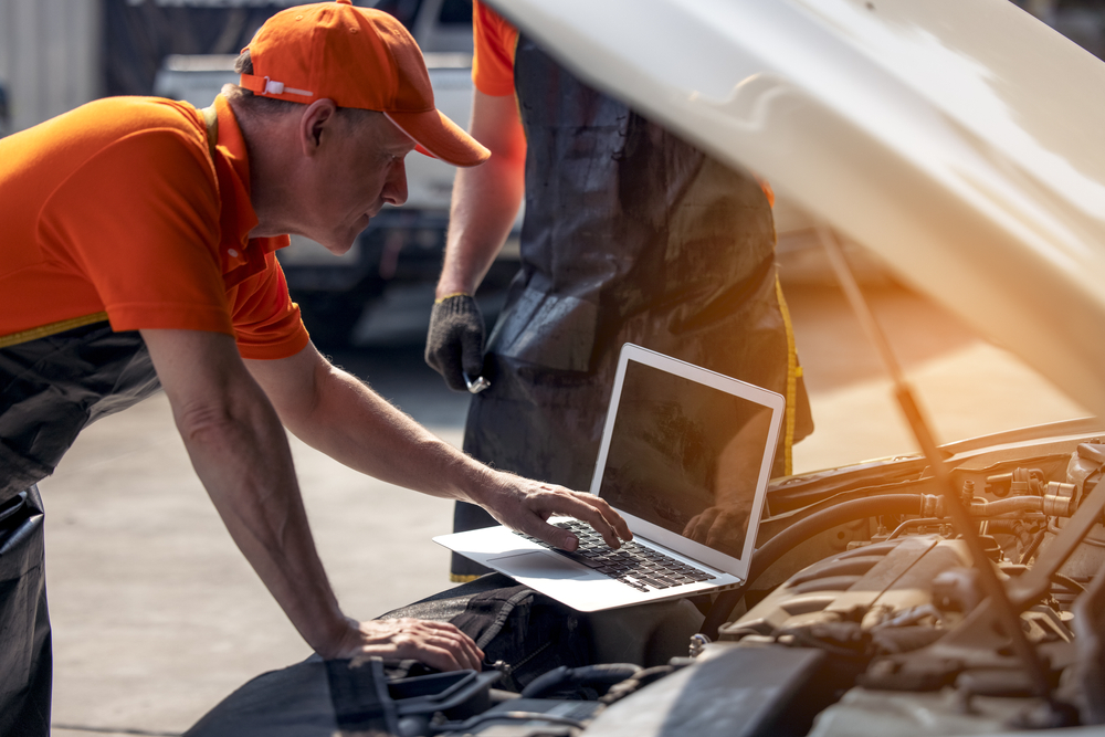 Diesel technician in an orange shirt diagnoses an engine problem with a laptop, example of diesel technician training