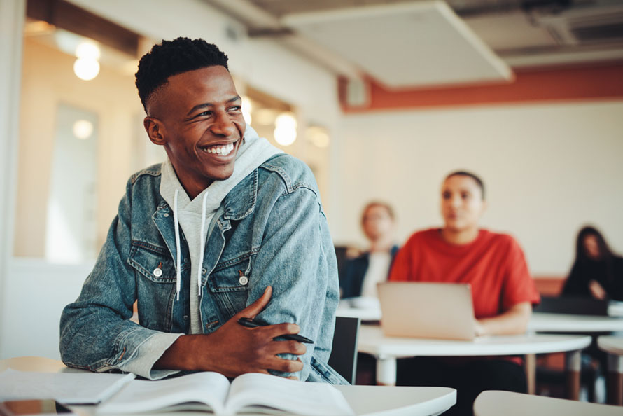 Black male teen smiles in class. Example of associate degree jobs that are not as well-known.