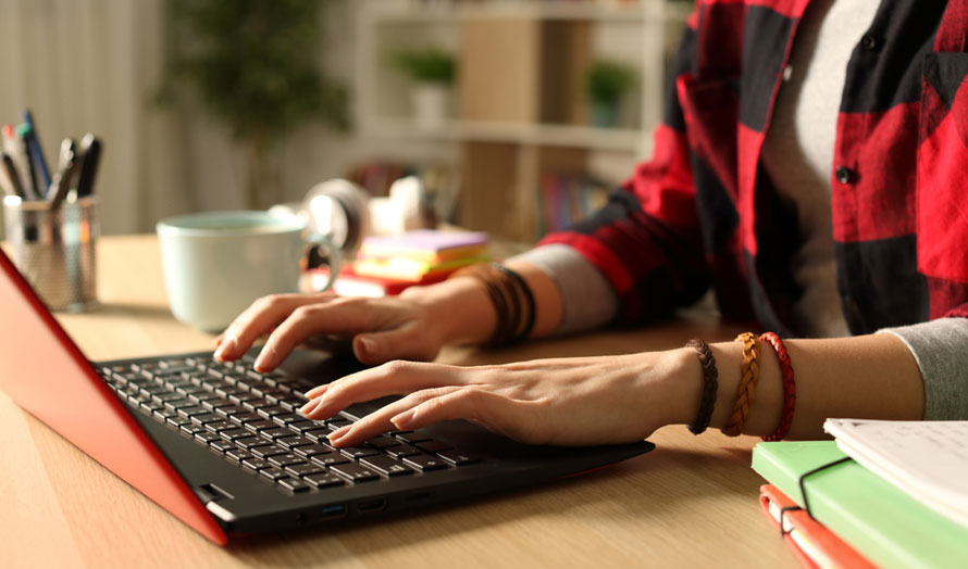 Close up of teenage girl's hands as she works on a laptop. Example of looking for trade school scholarships and how they support young people trying to explore skills-based jobs. 