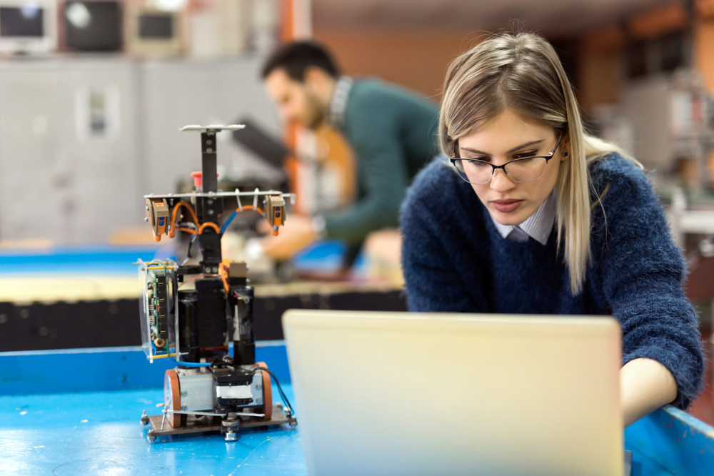 Young woman works on a computer for a robotics project, example of electronic technician training