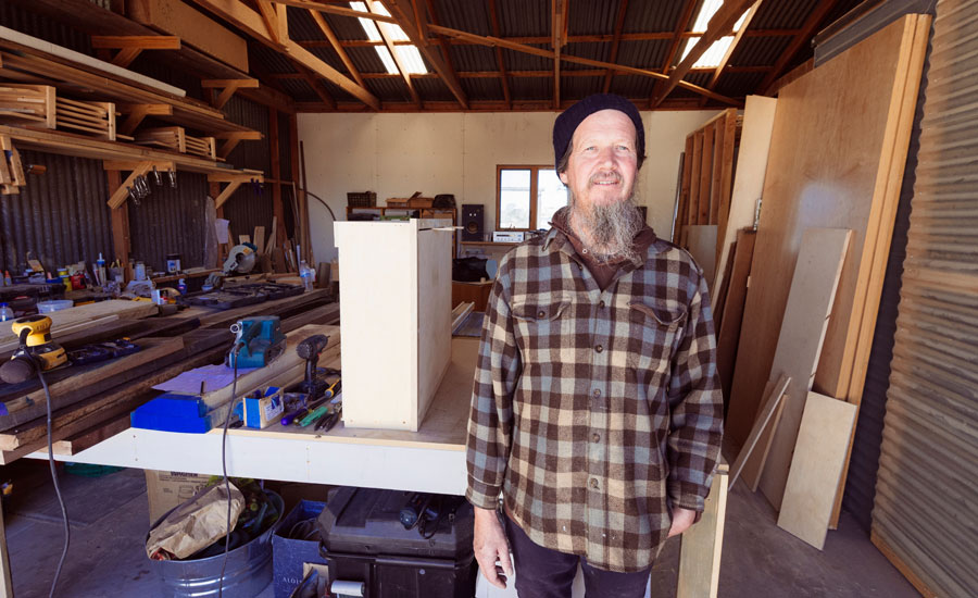 Carpenter with a beard stands in his woodworking shop
