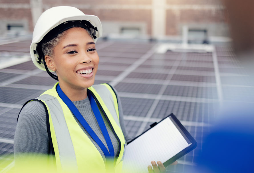 Young black woman with hardhat walks among a field of solar panels
