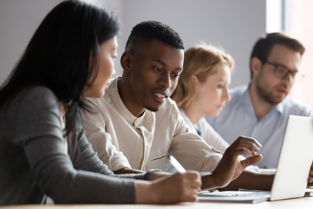 Black man and Asian woman look at laptop screen, example of on the job training in computer related job