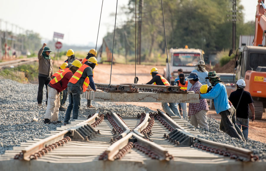 union construction workers help steer a new section of rail into place with the help of a crane