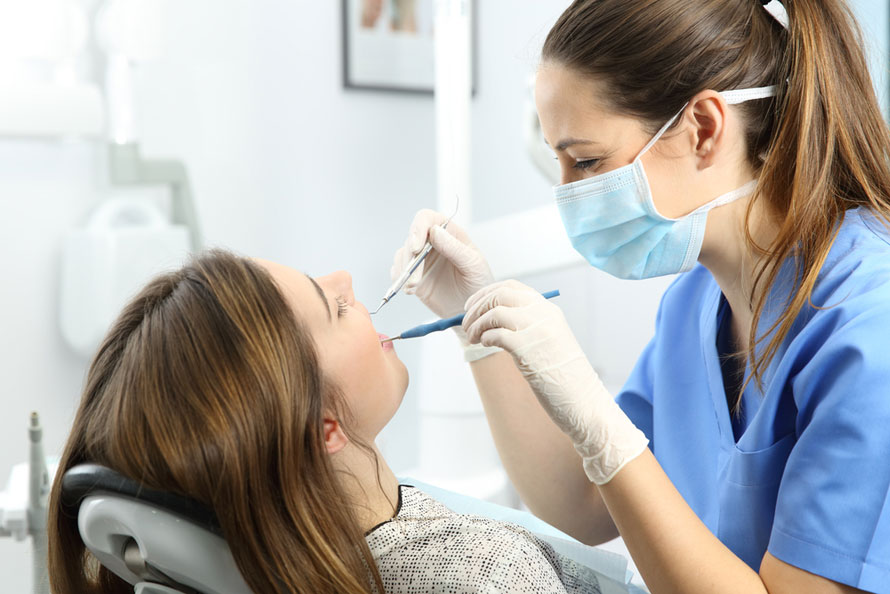 Young female dental hygienist cleans a patient's teeth. Example of associate degree jobs that pay well.