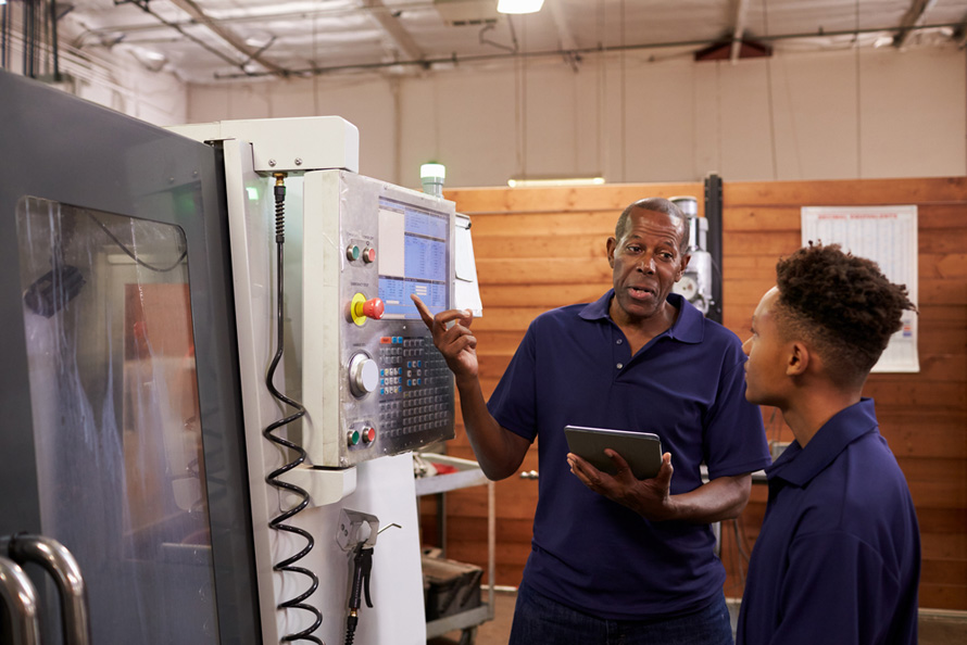 Black trainer works with black employee in advanced manufacturing setting. Example of micro credentials as a way to help solve the skills gap