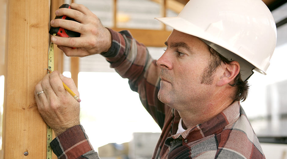 Carpenter with hardhat on measures and marks a wooden beam 