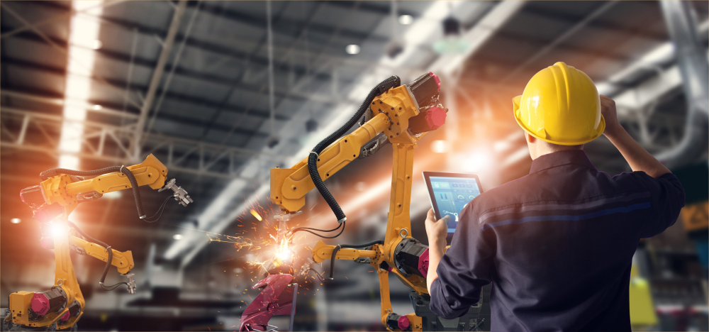 Man in hard hat watches a robotic arm in an auto factory, example of electrical technician training