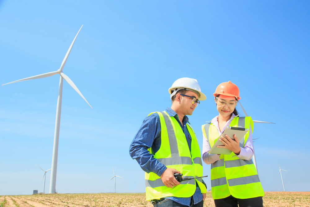two wind turbine technicians with safety equipment stand in front of a turbine