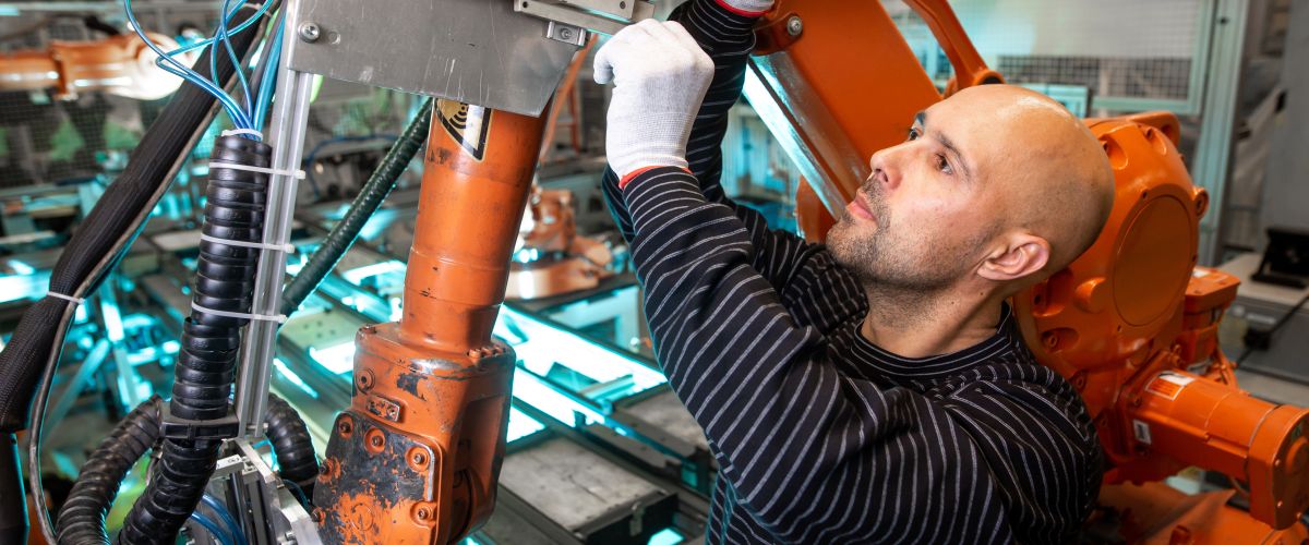 An industrial machinery mechanic does maintenance on an automatic robot arm in an auto factory