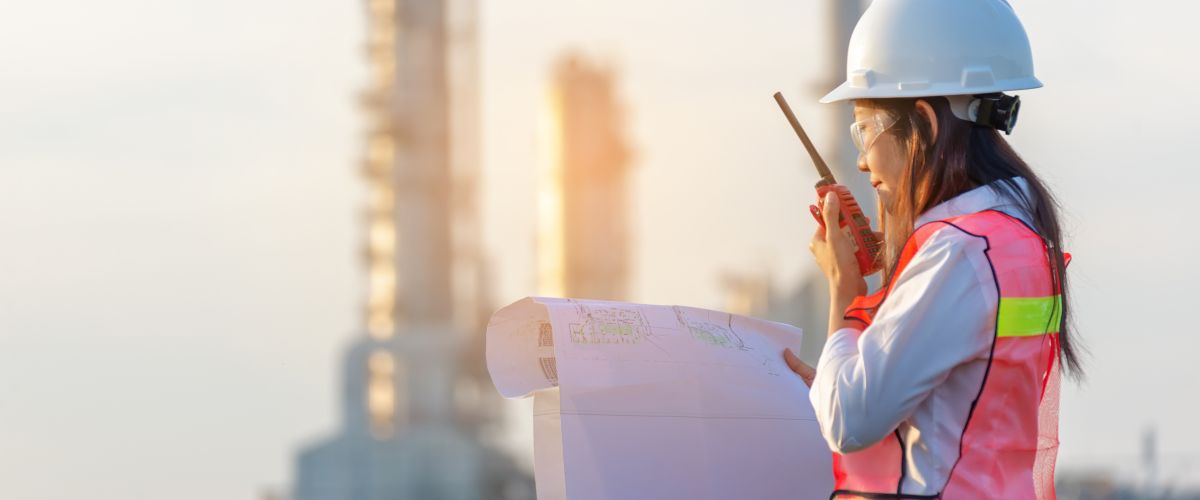 An industrial engineering technician reviews a blueprint in front of a worksite