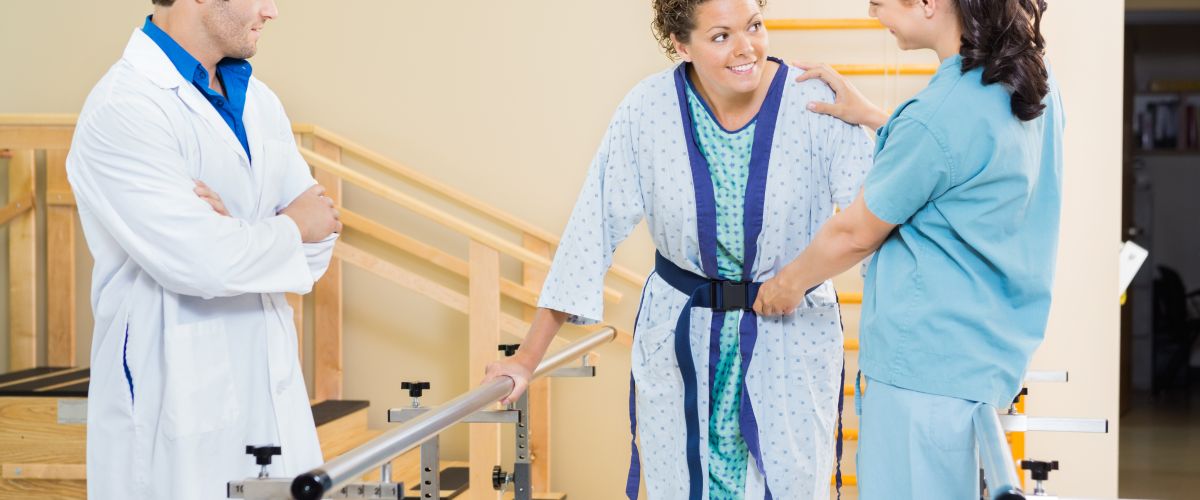 A physical therapy assistant helps a woman keep her balance as she tries to walk in the hospital