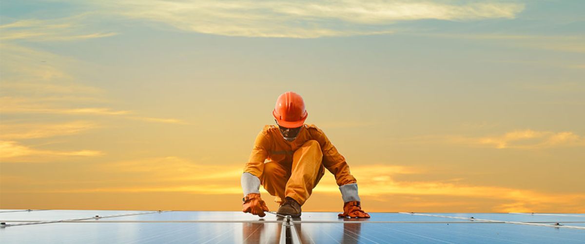 A solar technician installs solar panels with a sunset in the background