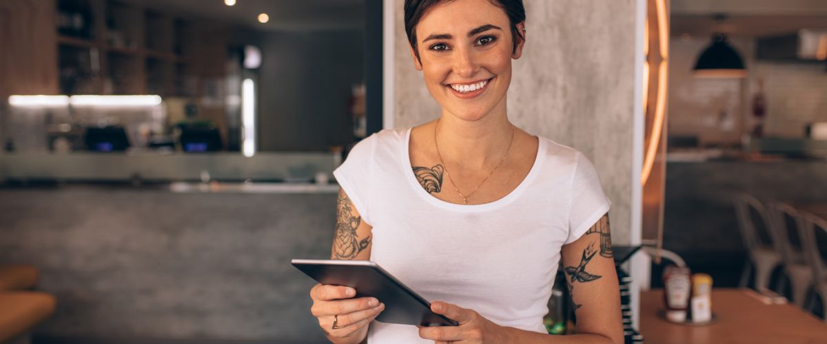 Young female food service manager with tattoos holding a tablet in a restaurant