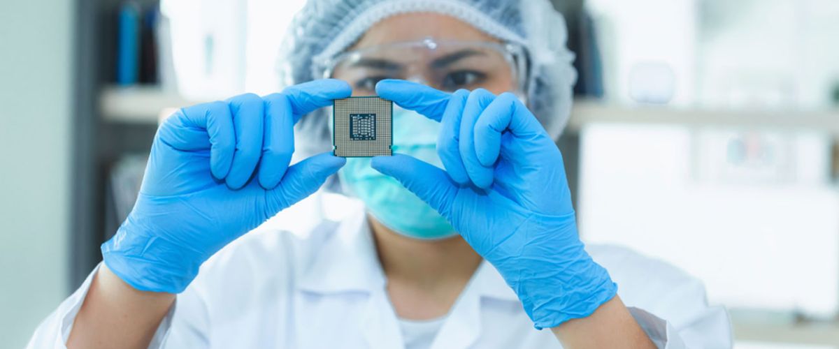 A female semiconductor technician wearing a clean suit examines an integrated circuit in a clean room in a manufacturing facility.