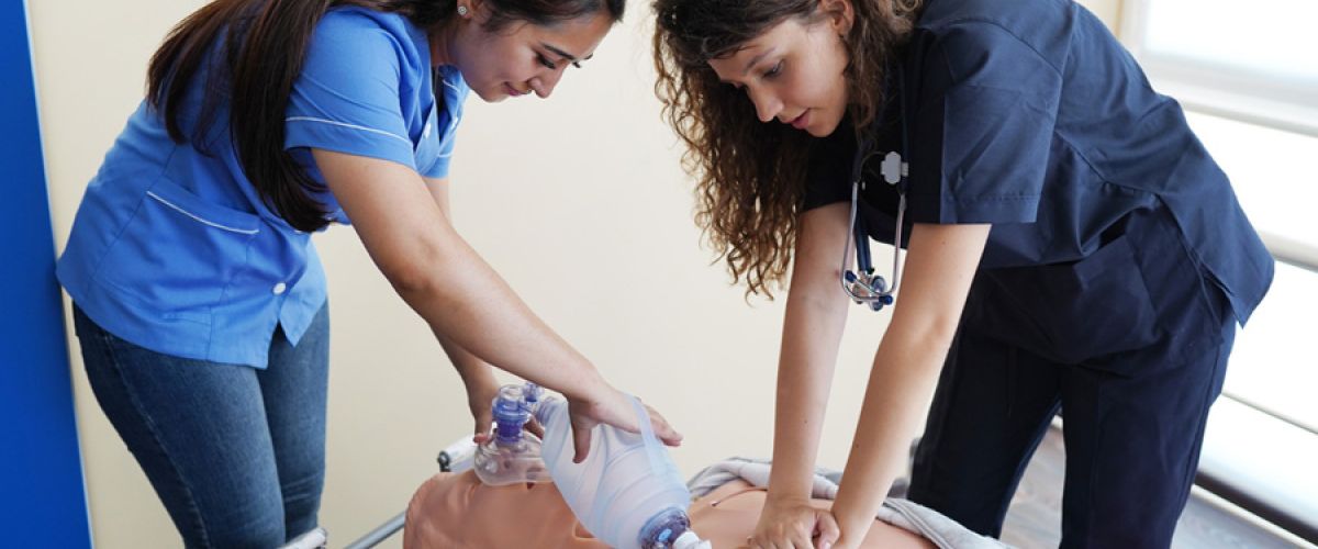 Two nursing students learn how to save real patients by practicing CPR on a dummy in a healthcare setting