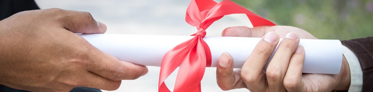 Two hands holding a rolled up piece of paper tied with a red bow.