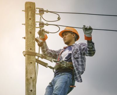 electrical lineman works with wires as they connect with the telephone pole