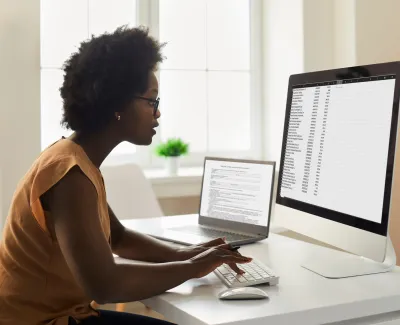 A young woman bookkeeper sits at a computer reviewing a ledger