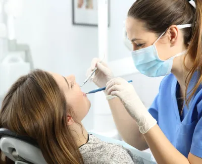 Young female dental hygienist cleans a patient's teeth. Example of associate degree jobs that pay well.