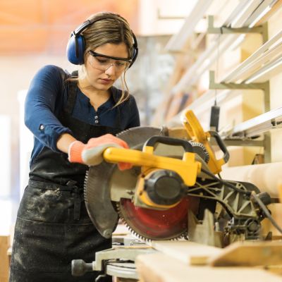 A female carpenter uses a miter saw to cut a piece of wood in the shop