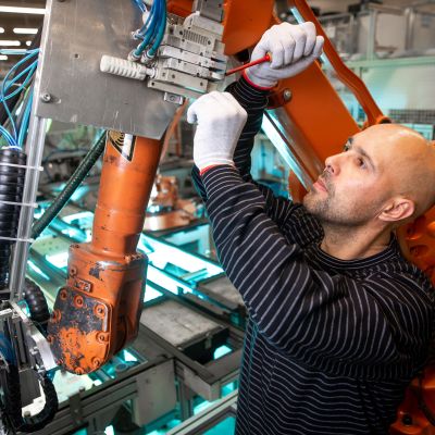 An industrial machinery mechanic or industrial maintenance technician does maintenance on an automatic robot arm in an auto factory