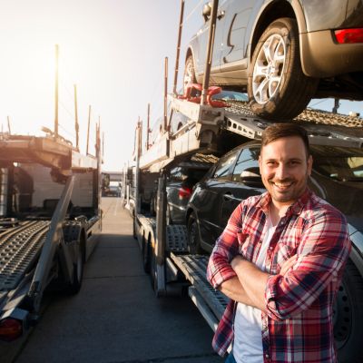 Truck driver stands in front of cars he is transporting to a dealership