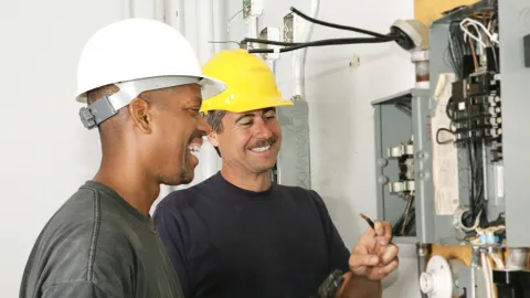 Two electricians work on an electrical panel. Electricians are among the good paying jobs that don't require a degree
