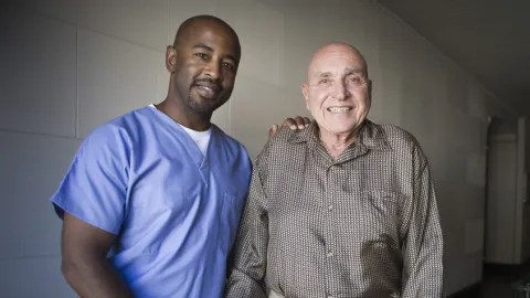 male certified nursing assistant helps patient get around with a walker