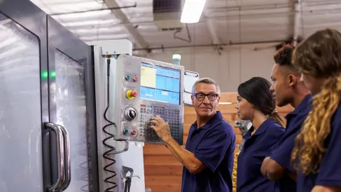 Machinist trains young apprentices on CNC machine