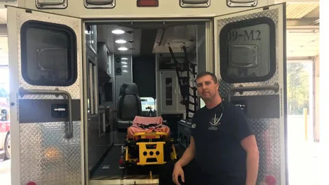 Paramedic Ryan Hollingsworth in front of the open doors of an ambulance