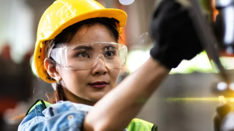 Woman worker wearing safety gear controls lathe machine, women in manufacturing and other skilled trade jobs