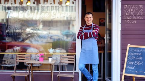 Proud young coffee shop owner stands in front of his tea and coffee shop